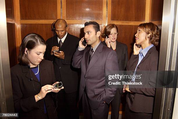 businesspeople using cellular phones in elevator - crowded elevator stockfoto's en -beelden