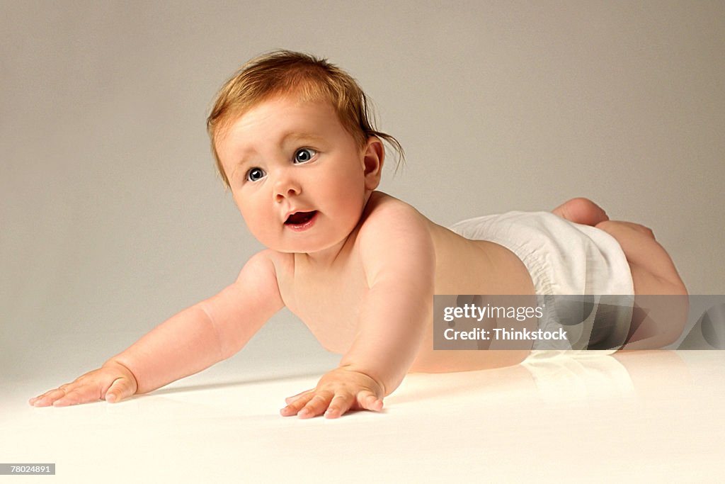 Portrait of a baby wearing a diaper lying on her belly and pushing up with her arms