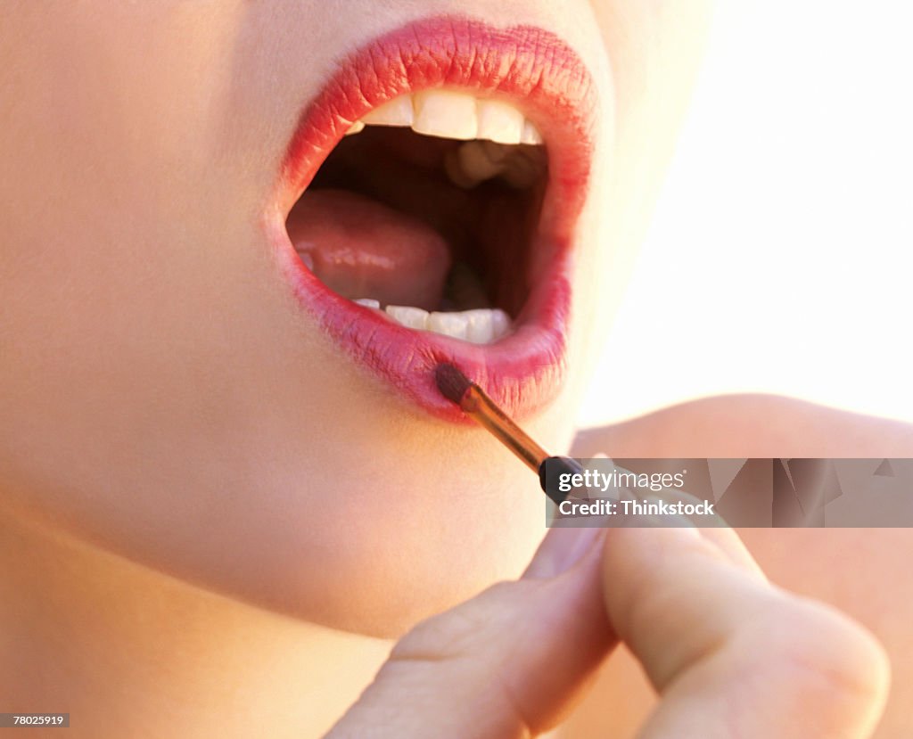 Close-up of a woman applying lipstick with a brush.