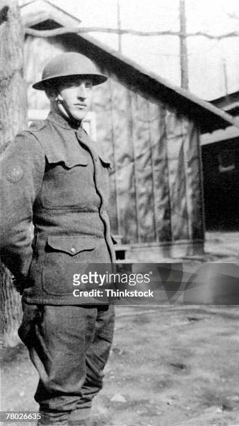 portrait of a military man in uniform with helmet standing near barracks; circa ww1. - world war one soldier stock pictures, royalty-free photos & images