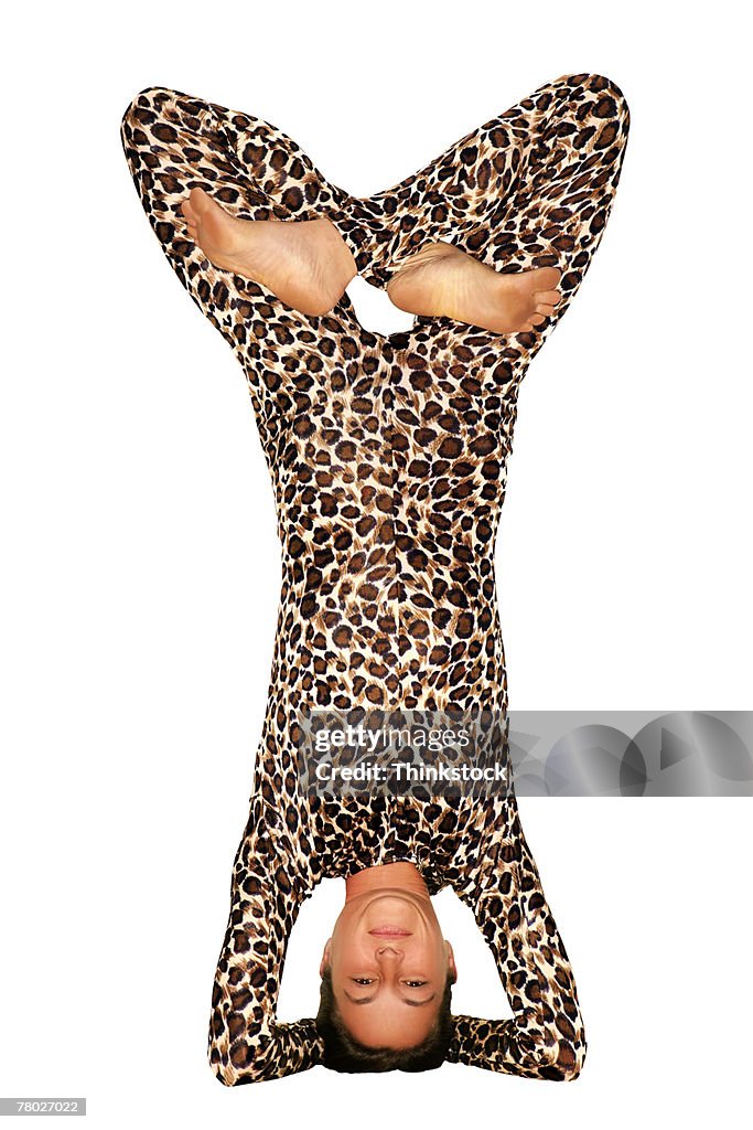 A woman in a leopard print unitard does a headstand with her legs crossed.