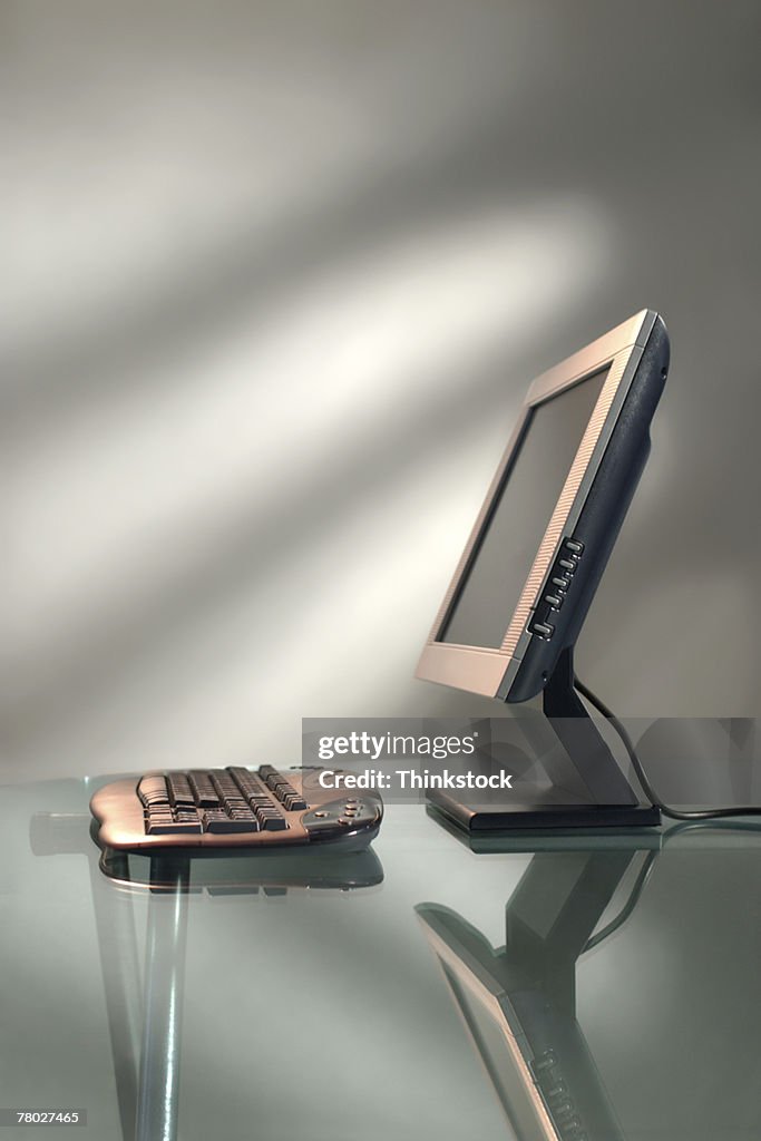 Still life side view of a flat screen monitor and a keyboard on a glass desktop