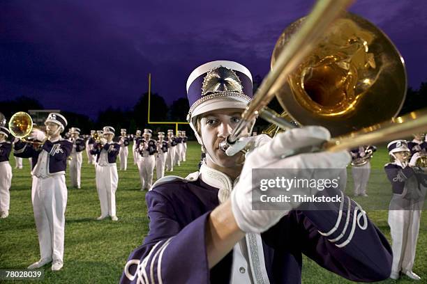 close-up of a band member playing his trombone with the marching band performing in the background. - banda de marcha fotografías e imágenes de stock