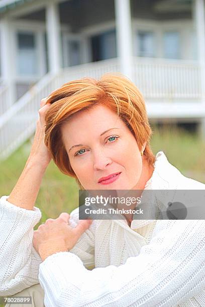 portrait of a woman sitting outdoors pulling her hair back with one hand and looking seriously at the viewer. - woman pulling hair back stock pictures, royalty-free photos & images