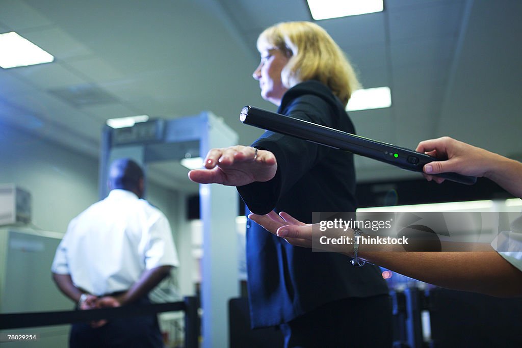 Close-up of an airport security officer using a hand held metal detector to check a traveler