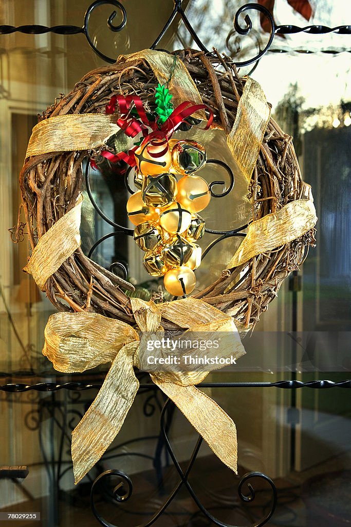 Close-up of a natural vine wreath wrapped in gold ribbon with brass bells on the front door for Christmas.