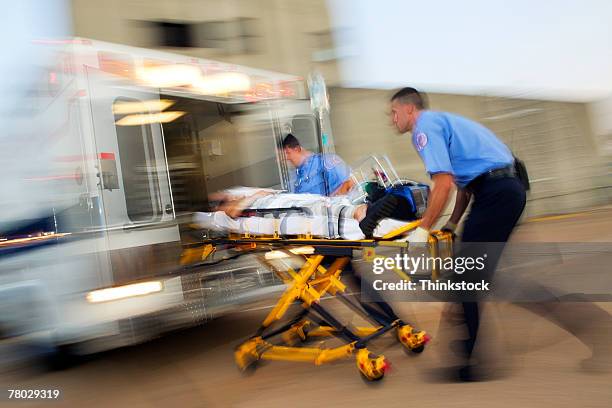 motion blur image of two medics loading a patient on a stretcher into the back of an ambulance - stretcher stock pictures, royalty-free photos & images