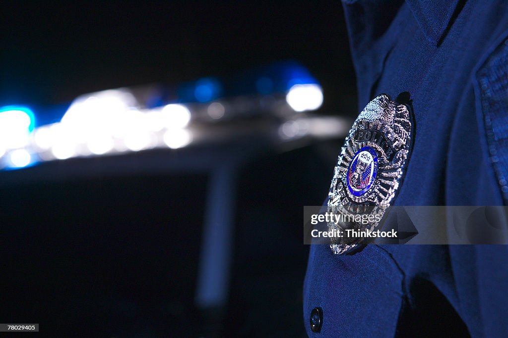 Close-up of an officer's badge with the police lights on the car flashing in the background