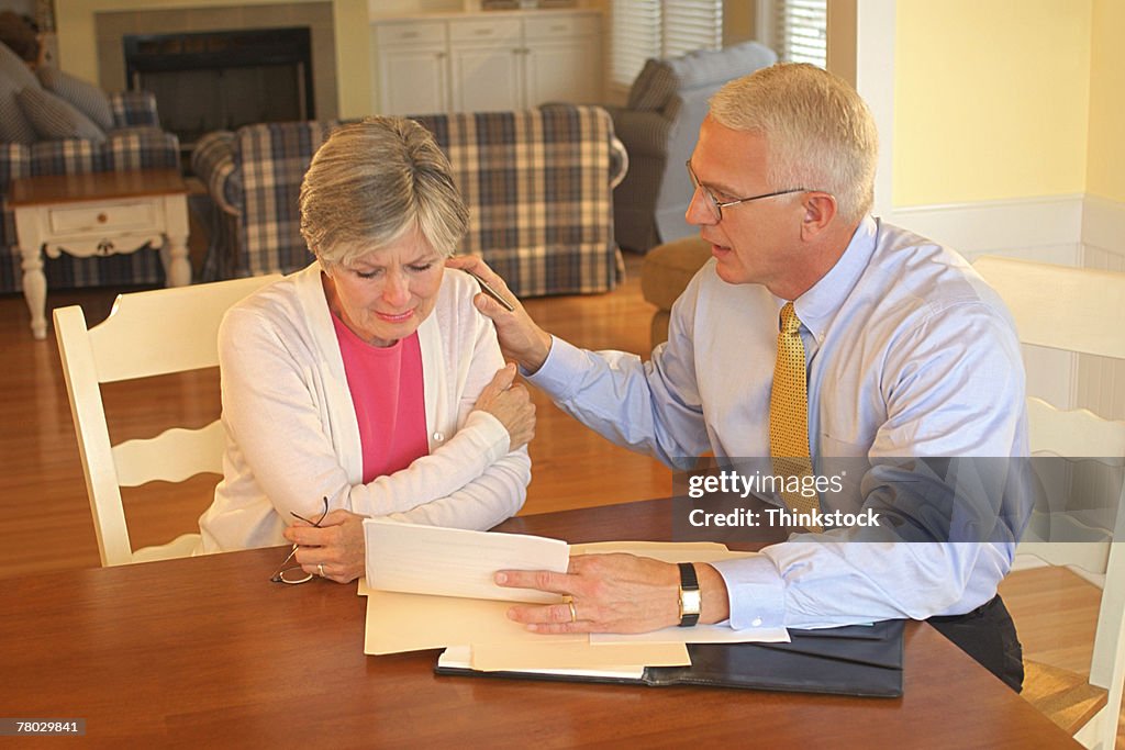 A businessman reassures a woman while discussing finances or legal matters in her home.