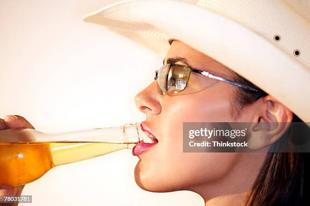 profile view of a woman wearing sunglasses and a cowboy hat as she drinks a beer out of a bottle - beer bottle mouth stock pictures, royalty-free photos & images