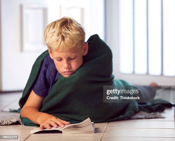 a boy lies on the floor wrapped in a blanket, reading a book - boy floor stockfoto's en -beelden