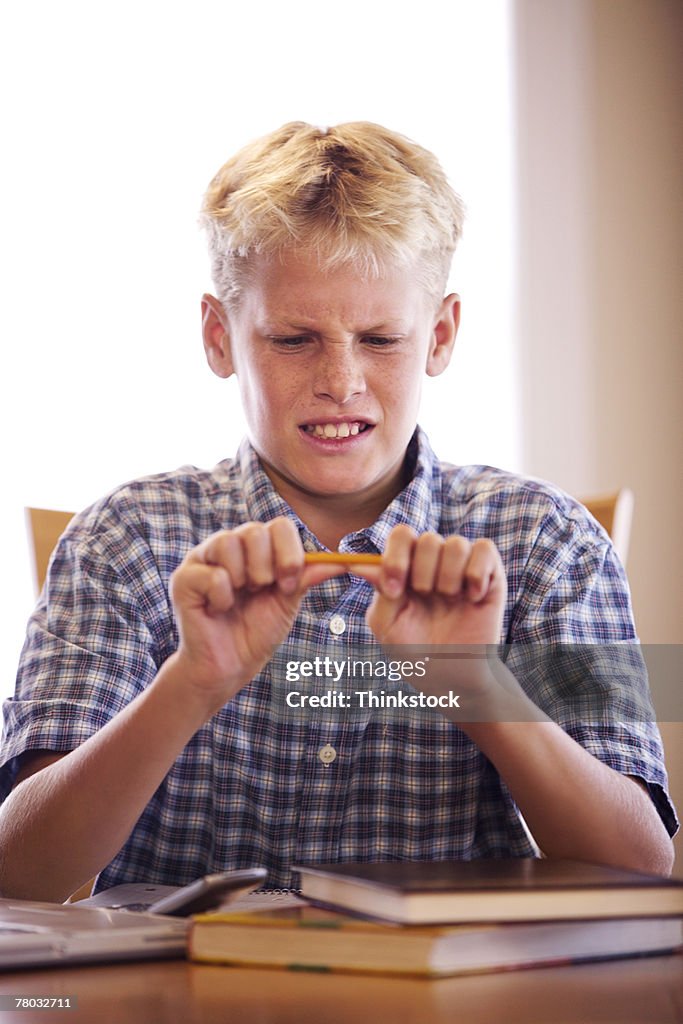 A boy breaks a pencil in frustration while doing his homework