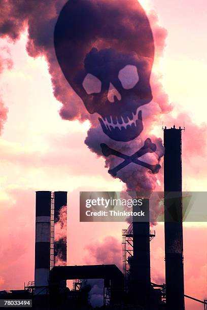 sepia tone of smoke billowing from industrial smokestacks composited with a skull and crossbones for warning. - bottone stockfoto's en -beelden