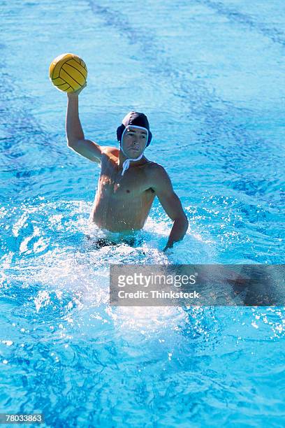 a water polo player lifts out of the water to pass the ball toward the viewer - male throwing water polo ball stockfoto's en -beelden