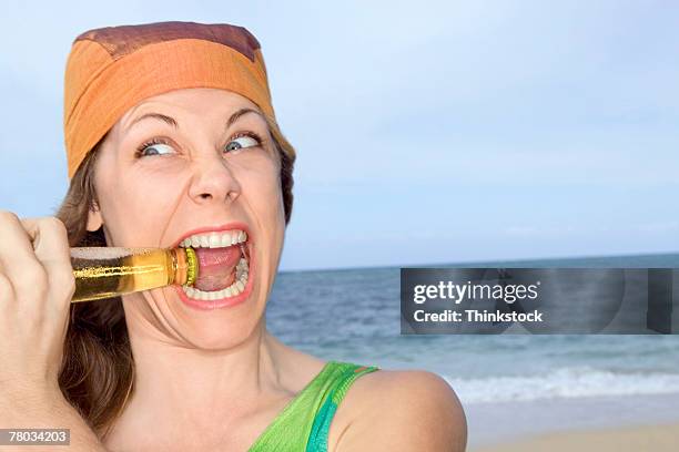 portrait of a woman at the beach biting the cap off of a bottle - beer bottle mouth stock-fotos und bilder