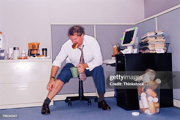 businessman sitting at messy desk scratching his leg - chaos büro stock pictures, royalty-free photos & images