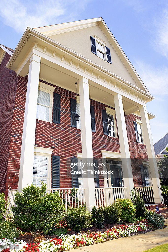 Low angle of a suburban brick house with columns and flowers in the front yard