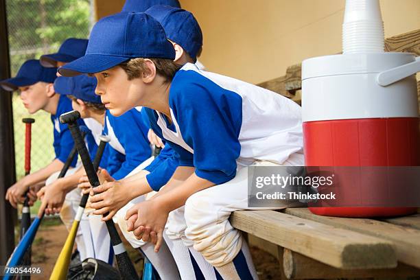 young baseball players sitting in dugout - banco de jogadores fotografías e imágenes de stock