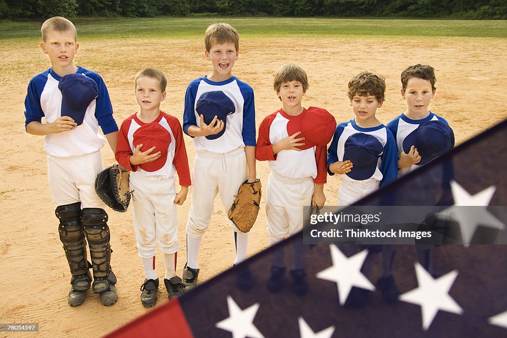 Young baseball players holding caps in front of American flag