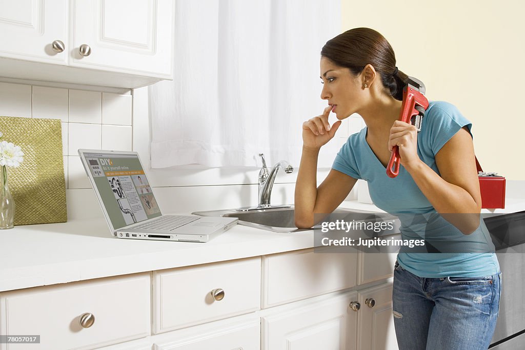 Woman holding monkey wrench and reading instructions on laptop