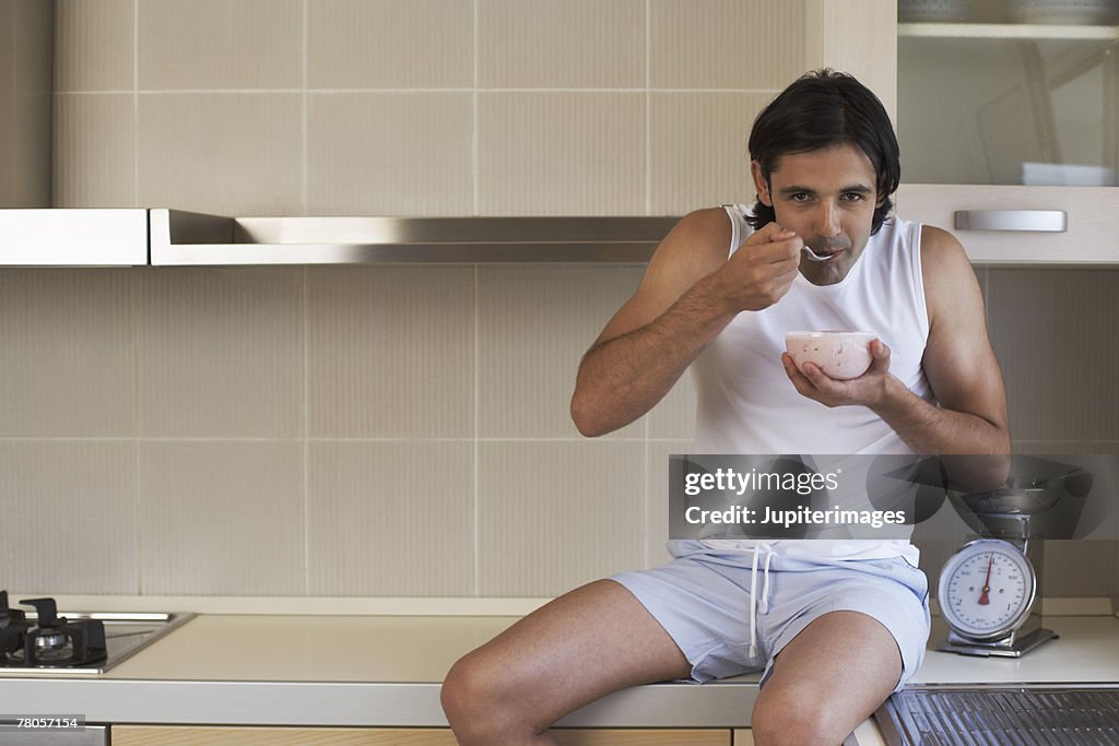 Man sitting on kitchen counter, eating yogurt and fruit