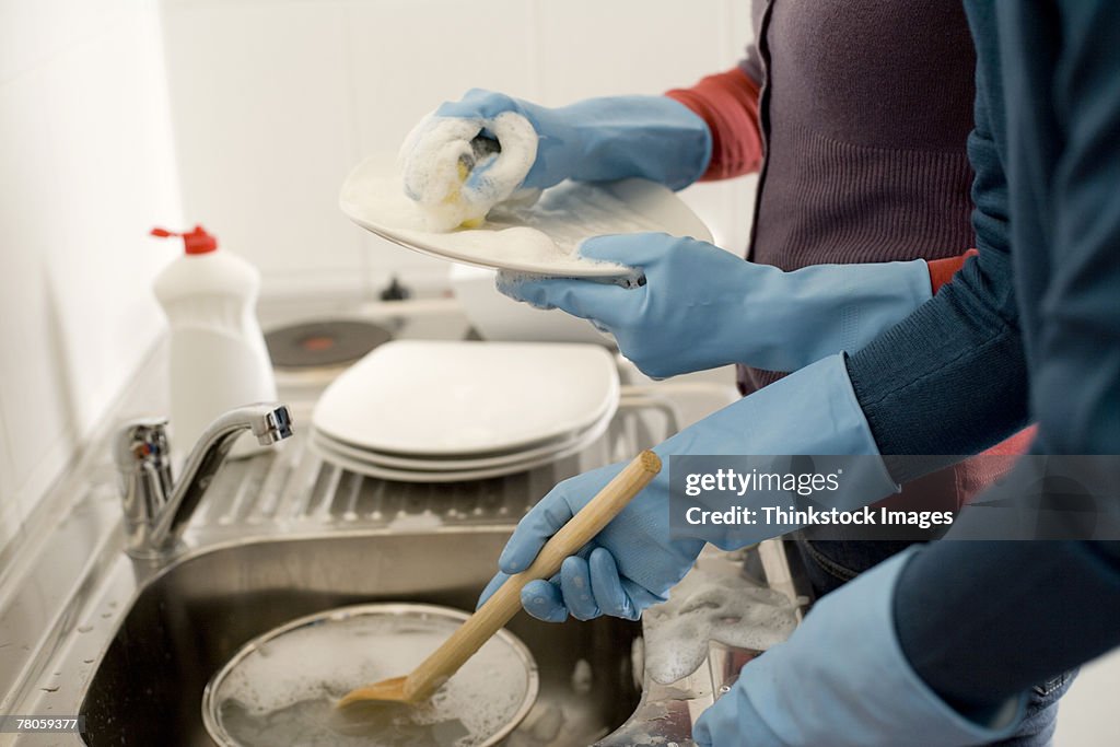 People's gloved hands washing dishes