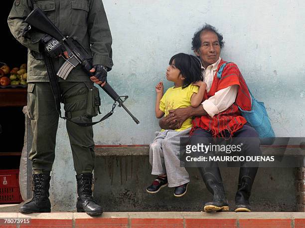 Colombian policeman stands guard next to a child and his father 08 June in Toribio, department of Cauca, Colombia. Policemen and soldiers kept on...