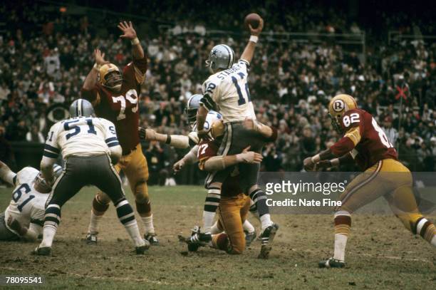 Hall of Fame quarterback Roger Staubach of the Dallas Cowboys throws a pass in spite of being in the grasp of Redskins defensive tackle Bill...