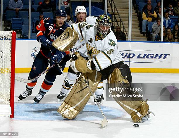 Goaltender Marty Turco of the Dallas Stars clears the puck from in front of the net as Miroslav Satan of the New York Islanders looks on during their...