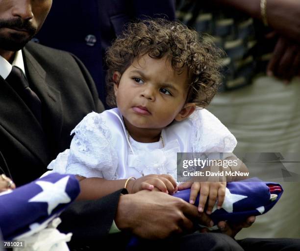 Preshilla Caprice Kumar, 18 months-old, holds the flag that covered her mother's coffin October 20, 2000 as she sits in the lap of her father,...