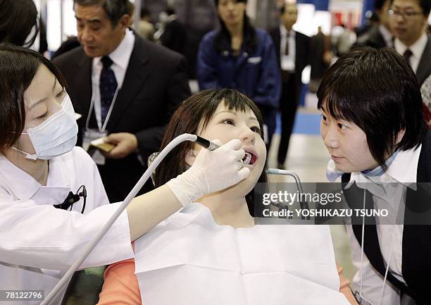 Visitor gazes at a humanoid robot dental therapy simulator "Simroid" for dentists and students, which has sensors in its mouth and shouts "Ouch" when...