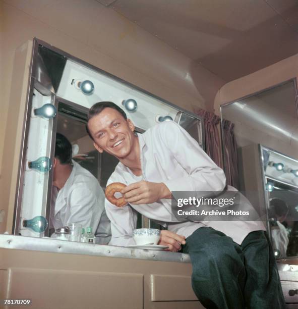 American actor and singer Frank Sinatra enjoys coffee and donuts in his trailer during a break in filming, circa 1950.