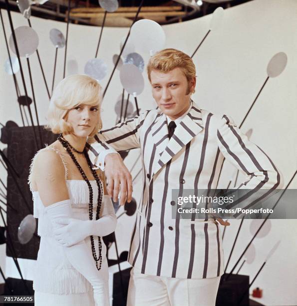 French husband and wife singers and actors Johnny Hallyday and Sylvie Vartan posed together wearing white flapper style period dress and white and...