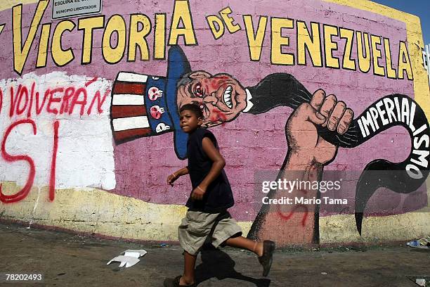 Boy runs past anti-American propaganda and graffiti reading "Si" signifying support for a referendum on changes to the Constitution introduced by...