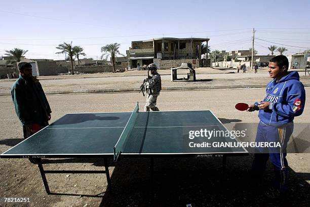 Soldier from Bravo company, 1st Battallion, 38 regiment infantry walks past Iraqis playing table tennis during a patrol at a market area in Baquba,...