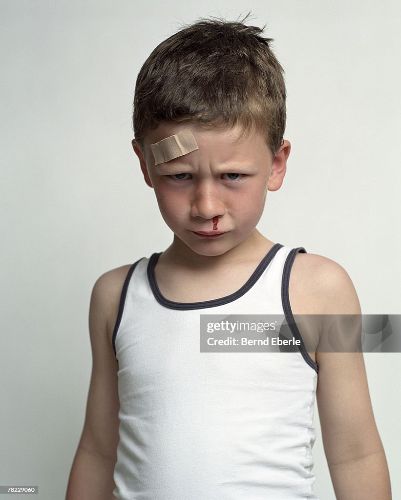 Desperate looking boy with plaster on his forehead, bleeding from the nose