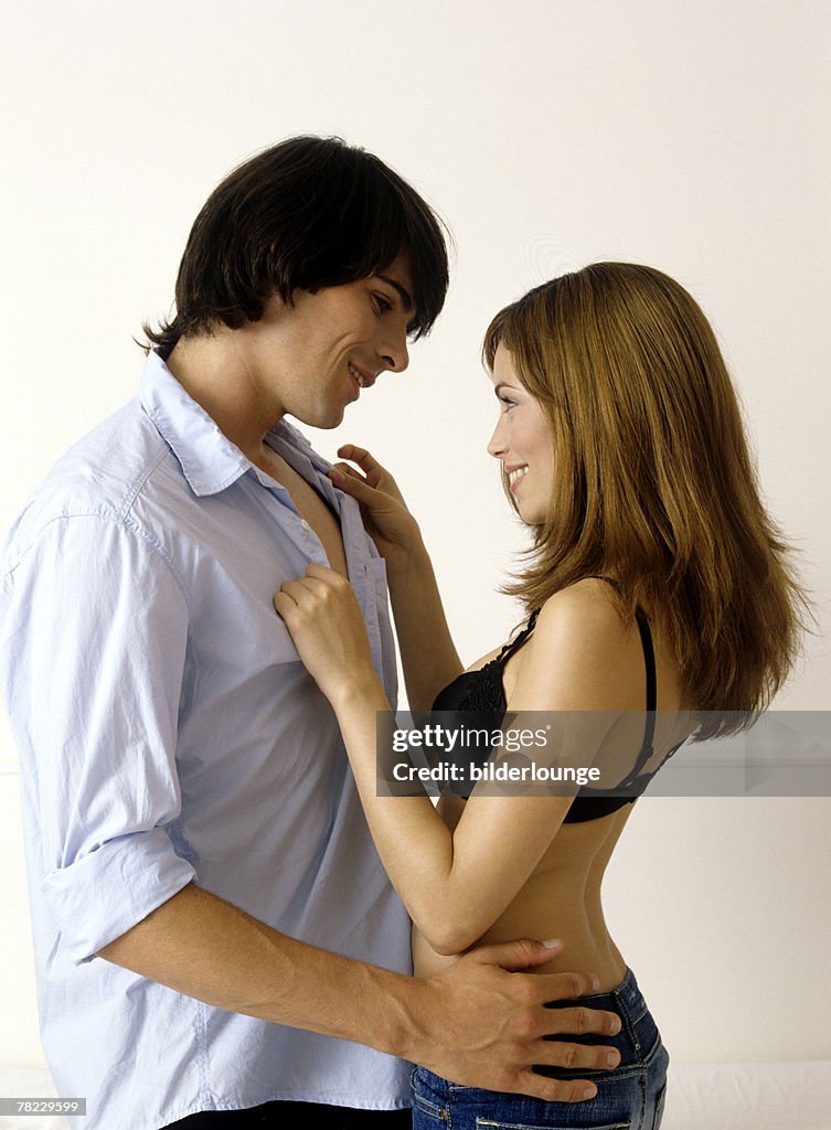 Young couple face to face, woman unbottoning shirt of man