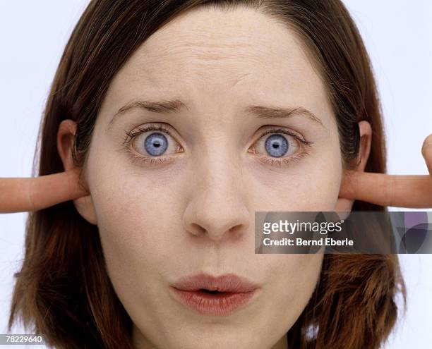 young woman putting her fingers into the ears - woman fingers in ears fotografías e imágenes de stock