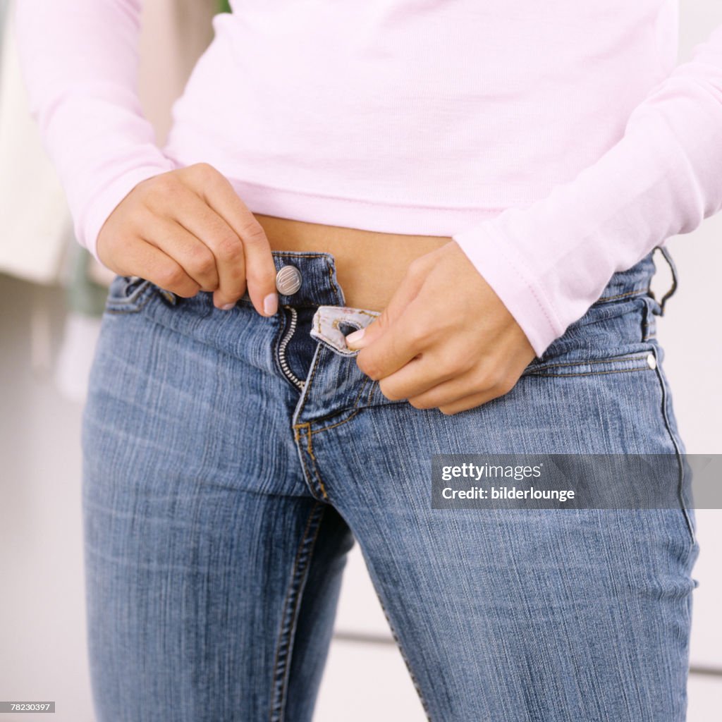 Close-up of young woman buttoning her blue jeans