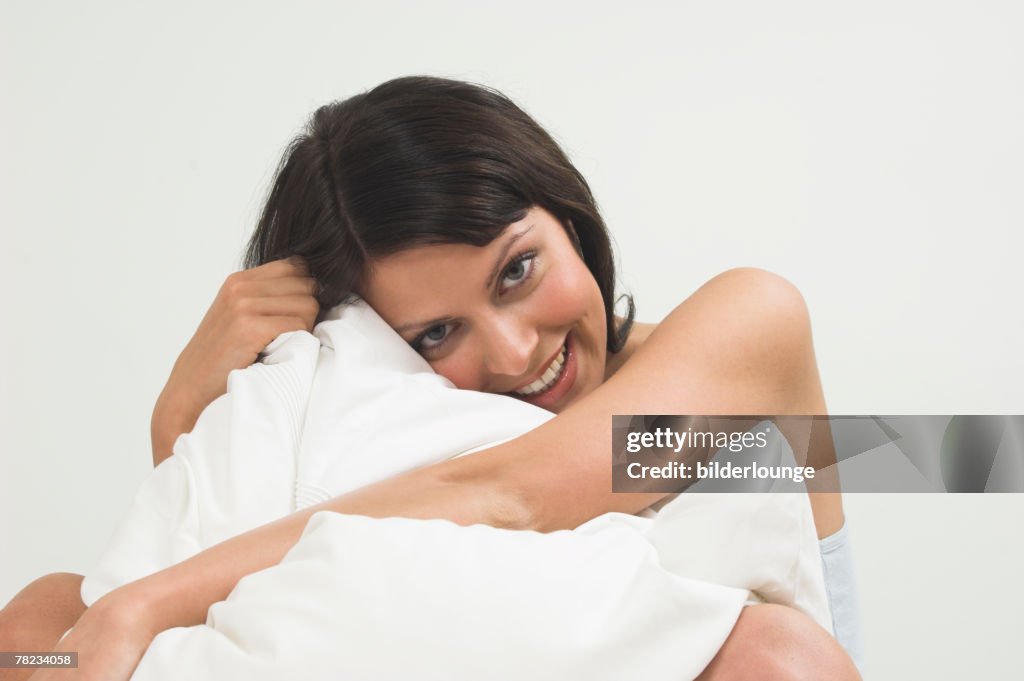 Portrait of young woman cuddling white pillow