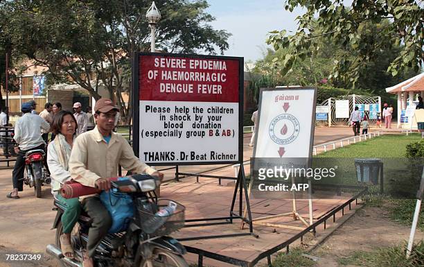 Couple rides by a sign warning of a Dengue fever epidemia next to a hospital 24 November 2007, near siem Reap, Cambodia. The World Health...