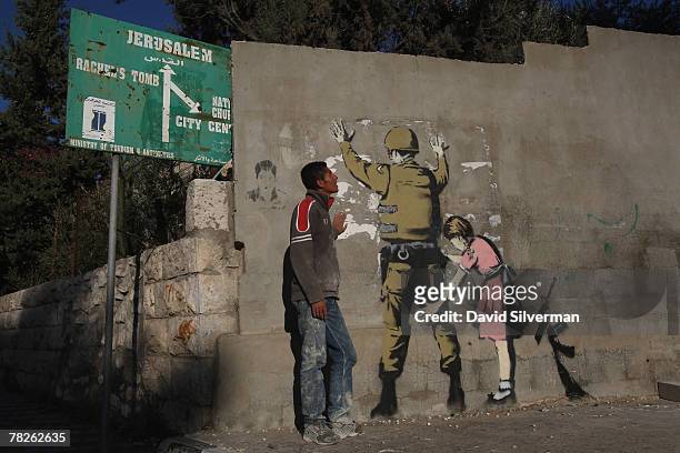 Palestinian labourer looks up at a wall painting by elusive British graffiti artist Banksy December 5, 2007 on a wall in the biblical city of...