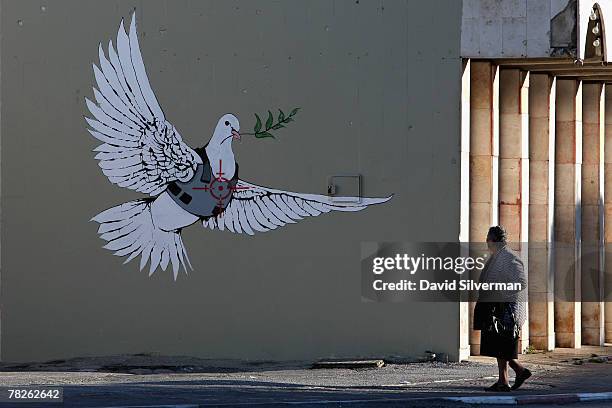 Palestinian woman pauses to look at a wall painting by elusive British graffiti artist Banksy December 5, 2007 on a shop wall in the biblical city of...