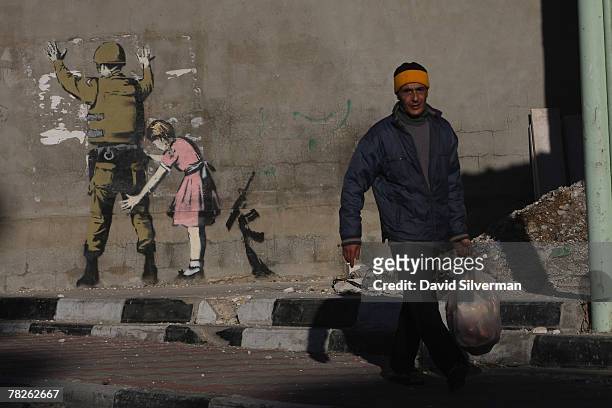 Palestinian passes a wall painting by elusive British graffiti artist Banksy December 5, 2007 on a wall in the biblical city of Bethlehem in the West...
