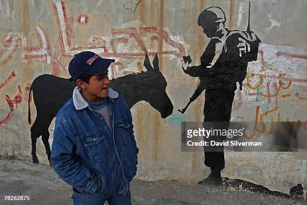 Palestinian youth passes a wall painting by elusive British graffiti artist Banksy December 5, 2007 on a shop wall in the biblical city of Bethlehem...