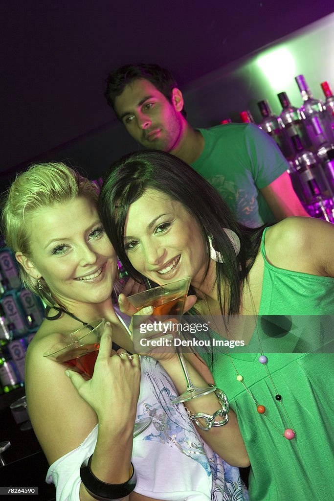 Portrait of two young women standing at a bar counter and holding martini glasses