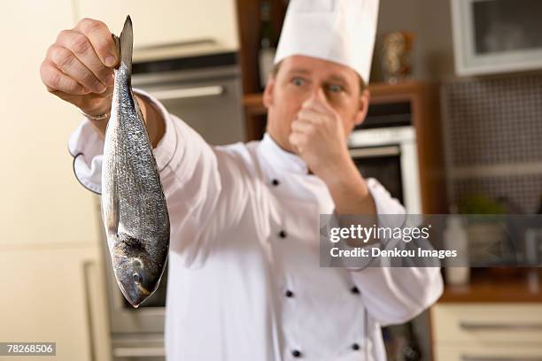 a chef holding a smelly fish - chef smelling food stockfoto's en -beelden