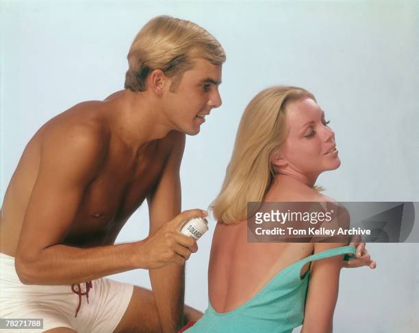 Male model in a swimming trunks prepares to spray an aerosol can of Solarcaine brand local anesthetic onto the sunburned back of his female...