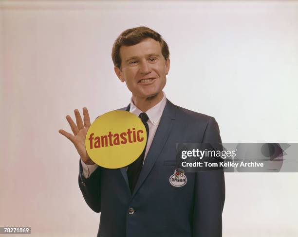 An unidentified model in a blue Alpha Beta grocery store blazer smiles enthusiastically as he holds up a large yellow disc that reads, in red...