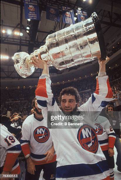 Surrounded by teammates, Canadian ice hockey player Duane Sutter of the New York Islanders holds aloft the Stanley Cup on the ice after his team's...